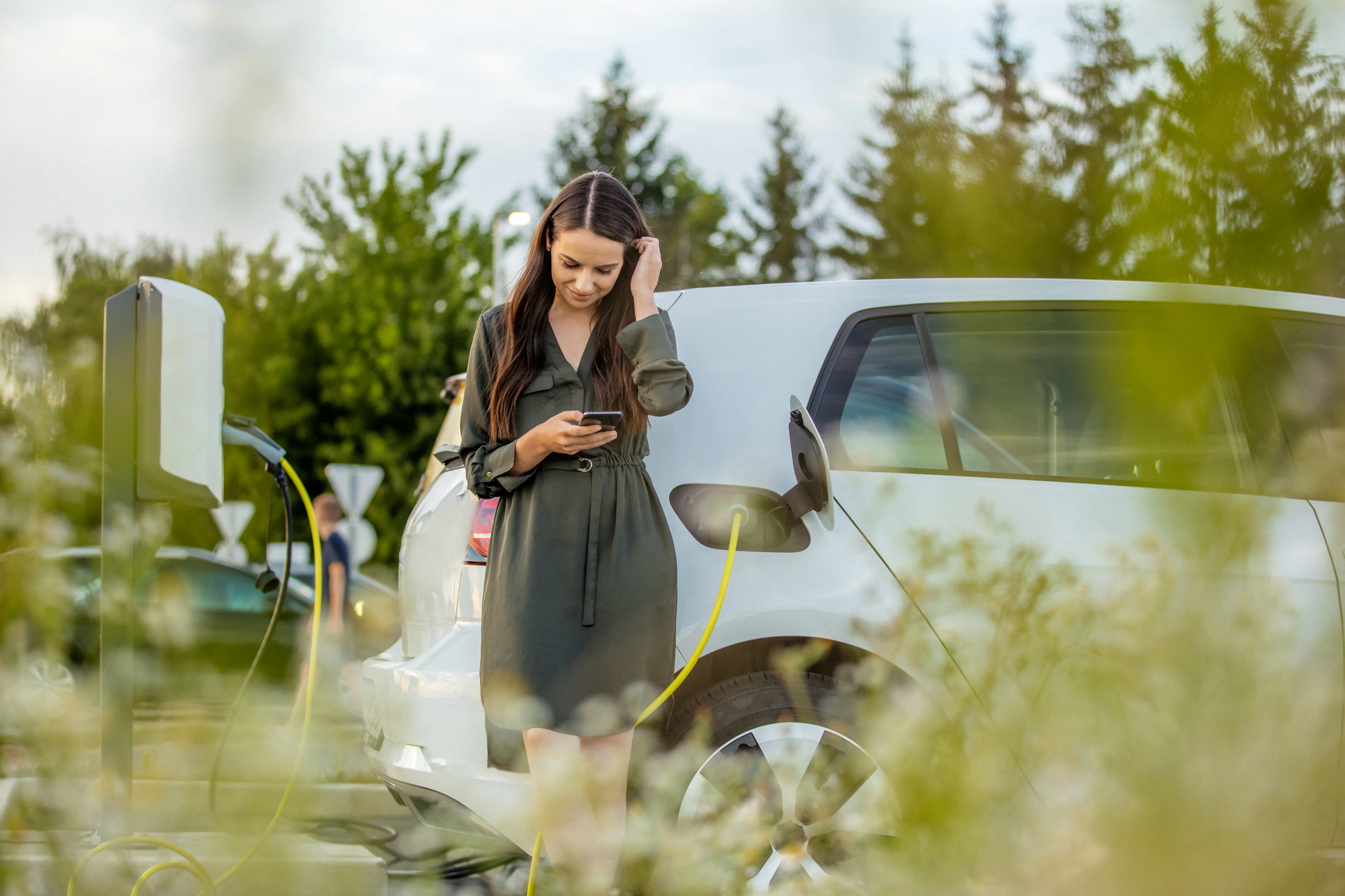 woman learning against charging electric car