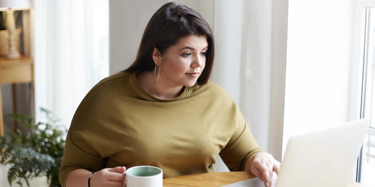 woman working on laptop at desk holding mug