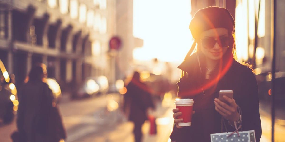 woman in street holding a takeaway coffee and looking at mobile phone